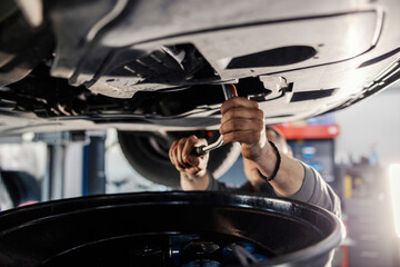 Wall Mural - Close up of a mechanic using offset spanner on a car while standing under it at mechanic's shop.