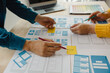 © Witoon - Close up ux developer and ui designer brainstorming about mobile app interface wireframe design on table with customer breif and color code at modern office.Creative digital development agency