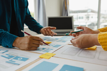 Close up ux developer and ui designer brainstorming about mobile app interface wireframe design on table with customer breif and color code at modern office.Creative digital development agency