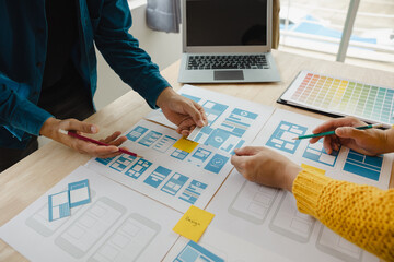 Close up ux developer and ui designer brainstorming about mobile app interface wireframe design on table with customer breif and color code at modern office.Creative digital development agency