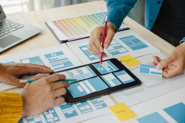Close up ux developer and ui designer brainstorming about mobile app interface wireframe design on table with customer breif and color code at modern office.Creative digital development agency