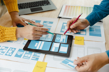 Close up ux developer and ui designer brainstorming about mobile app interface wireframe design on table with customer breif and color code at modern office.Creative digital development agency