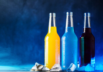 Wall Mural - bottled cold berry and fruit soda. blue background. cold summer drinks. ice cubes, copy space
