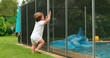 © Marco - Baby leaning on swimming pool fence protection. Infant standing on safety gate