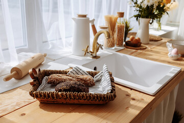 Fresh bread and utensils on the kitchen table, ready to be cooked. Simple modern scandinavian style kitchen, kitchen details, wooden table, bouquet of flowers in a vase on the table.