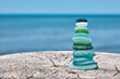 Balanced pyramid of sea-polished glass bottle shards on a weathered wooden surface against the backdrop of the sea