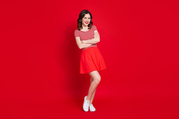 Full body photo of adorable youngster girl posing camera arms crossed wear cute crop top skirt sneakers isolated red color background