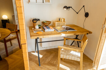 interior view of workspace with wooden table, shelves with books and lamp in stylish studio aparteme