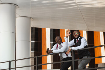 Sticker - Portrait of two dark-skinned businessmen talking in the background of a modern building exterior. Friendly meeting outdoors