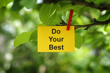 A yellow paper note with the phrase Do Your Best on it attached to a tree branch with a clothes pin