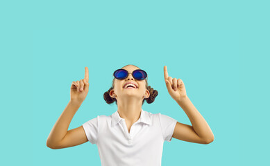 cheerful little caucasian girl teenager in funny sunglasses looks up in amazement pointing fingers a