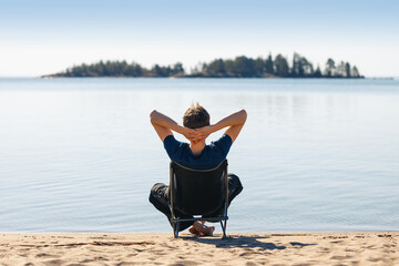 A man is resting in a camping chair on the seashore.