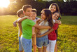 © Studio Romantic - Group of friendly cheerful children standing in circle and hugging each other on nice sunny day spend time together with classmates posing on lawn of summer park. School holidays concept