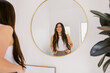 © ByLorena/Stocksy - Happy woman looks at herself in mirror at home