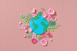 © Marc Tran/Stocksy - Globe with paper colorful flowers and leaves on a pink background.