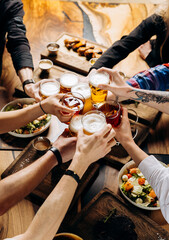 friends cheering beer glasses on wooden table covered with delicious food - top view of people havin