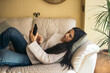 © Pedro Merino/Stocksy - Relaxed woman at home using smartphone lying on sofa