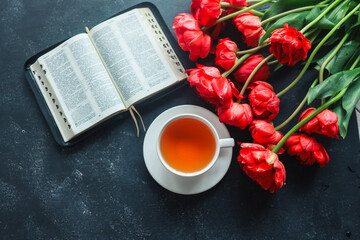 Wall Mural - Open bible with tulip flowers and a cup of tea on a dark background