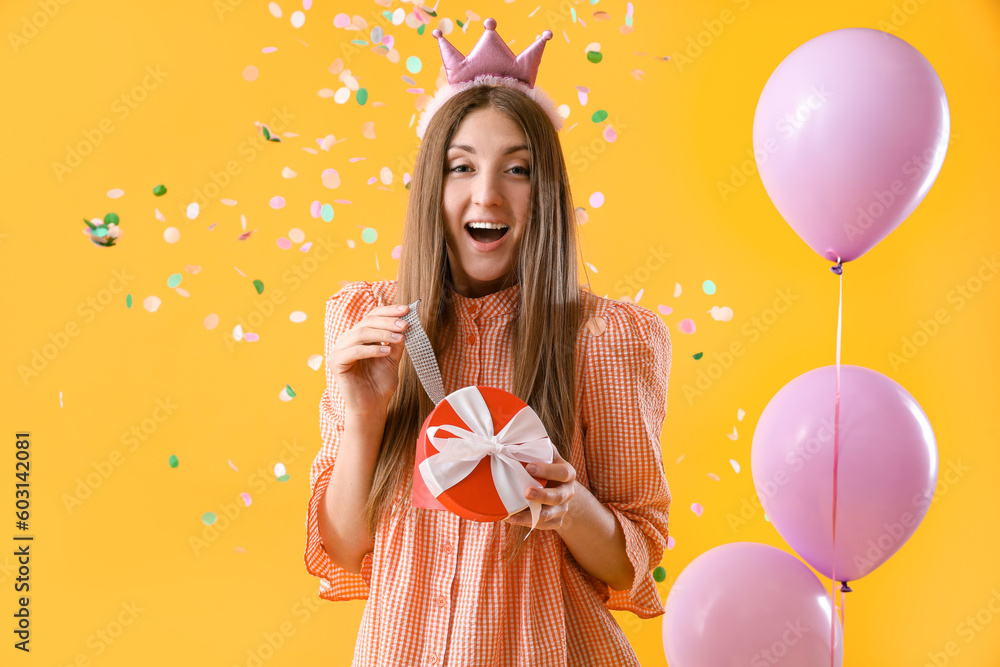 Surprised young woman with Birthday gift on yellow background