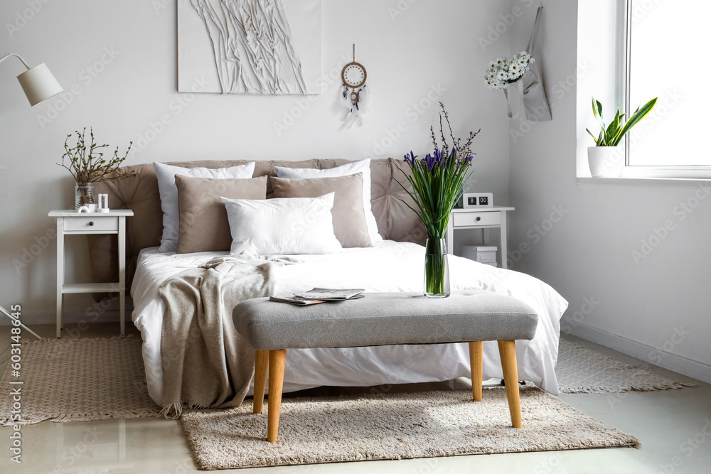 Interior of bright bedroom with beautiful iris flowers on bedside bench