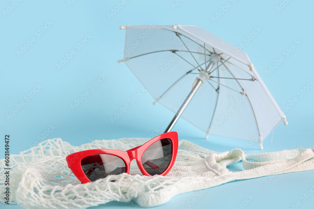 Sunglasses with string bag and umbrella on blue background