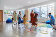 © .shock - Small nursery school children with female teacher on floor indoors in classroom, doing exercise. Jumping over hula hoop circles track on the floor.