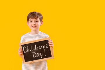 Little boy holding chalkboard with text CHILDREN'S DAY on yellow background