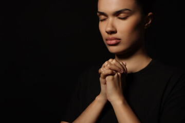 Wall Mural - African American woman with clasped hands praying to God on black background. Space for text