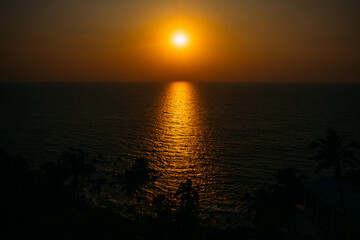  A bright misty sunset over the endless sea. Bright sunny path on the water and silhouettes of palm trees. Postcard view of a vacation near the sea, romantic meetings, background for travel