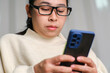 © Pornpimon - Happy young woman using mobile phone while sitting on sofa at home. Attractive woman holding smartphone checking social media, playing games, online shopping relaxing on sofa.