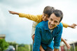 © Camerene P/peopleimages.com - Portrait, children and a son on back of his dad outdoor in the garden to fly like an airplane while bonding together. Family, kids and a father carrying his boy child while playing a game in the yard