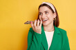 © sementsova321 - Laughing positive woman wearing green jacket posing isolated over yellow background recording voice message smiling happily copy space for promotion.
