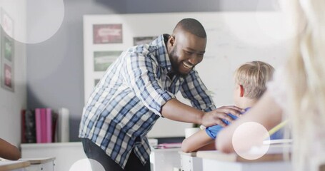 Poster - Animation of light spots over happy african american male teacher congratulating schoolboy at desk