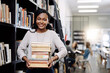 © Jadon Bester/peopleimages.com - Black woman, student with book stack in library and research for project, study and learn on university campus. African female person smile in portrait, education and scholarship with course material