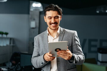 Poster - Young successful businessman working on digital tablet while standing in office