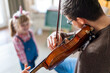 Charming little girl learning to play the violin with an artistic music teacher.