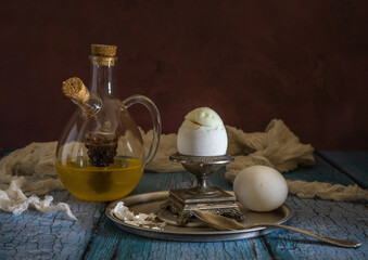 Two white chicken eggs, an egg cup and a decanter with olive oil and vinegar.