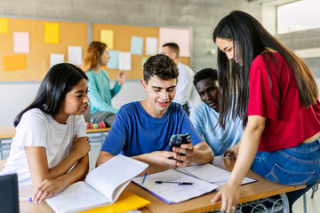 Multiracial group of student friends watching social media content on smartphone during the break in college classroom