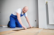 © anatoliy_gleb - Male construction worker laying laminate wooden plank on floor underlayment. Man in work overalls kneeling down by the wall and installing laminate flooring in living room. Home renovation concept.