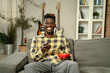 © JustLife - Young man watching tv at home. African sitting on the sofa, enjoy at home.