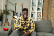 © JustLife - Young man watching tv at home. African sitting on the sofa, enjoy at home.
