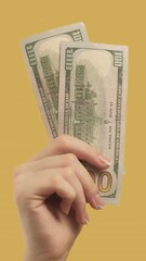 Wall Mural - Vertical video. Money gesture. Profitable investment. Woman hand with doubled 100 dollar note on yellow background.