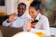 © Studio Marmellata - Cheerful adult Ethiopian couple in smart clothes smiling and waving hands while talking to friend on laptop at home together