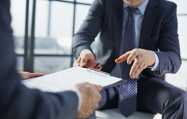 Two businessmen are sitting on chairs in the office while closing a deal.