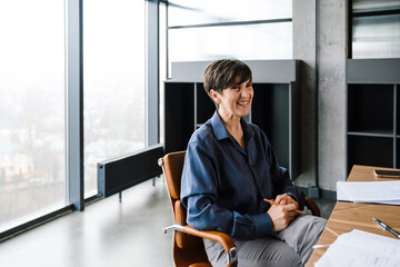 Professional elderly smiling businesswoman sitting at desk at office meeting 