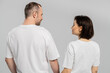 © LIGHTFIELD STUDIOS - back view of cheerful and tattooed woman with short brunette hair looking at husband with bristle while standing together in white t-shirts isolated on grey background, happy couple