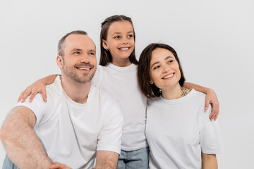 Wall Mural - stylish family in white t-shirts looking away while posing together on grey background, International child protection day, preteen daughter hugging happy parents