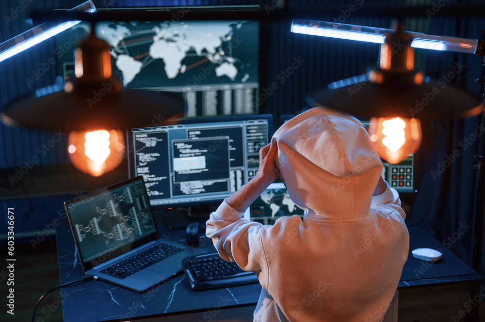 View from behind. Young professional female hacker is indoors by ...