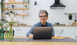 © Andrii Zastrozhnov - Mature woman working on a laptop in a home interior on the background of the kitchen.