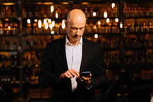 Portrait Of A Mature Gentleman, A Man In An Evening Restaurant With A Phone. A Man Writes A Message On A Smartphone
